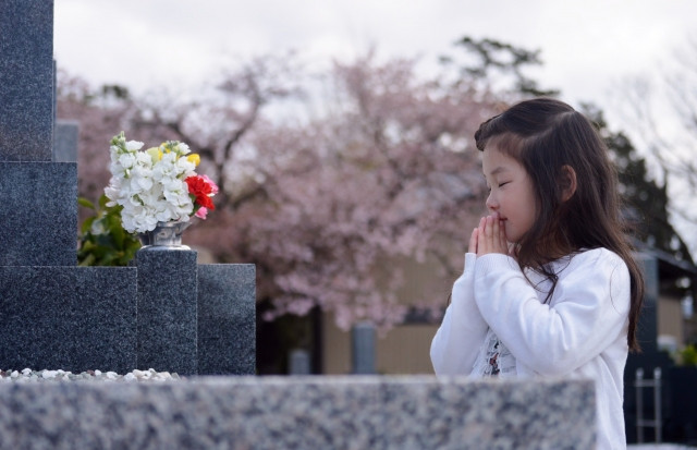 お墓の前で手を合わせ目を閉じる少女